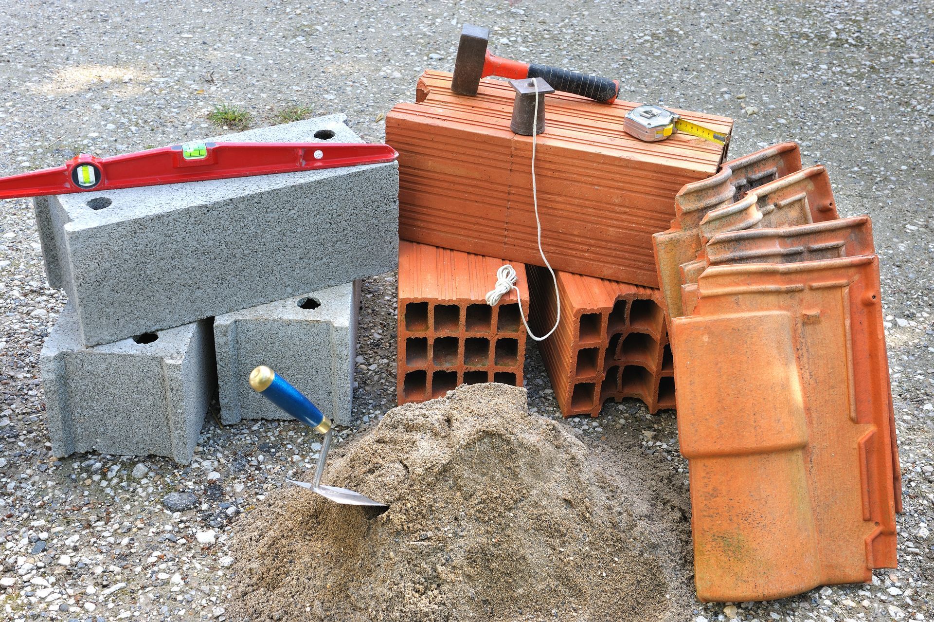 Matériaux de construction divers et blocs de maçonnerie empilés à l'extérieur sur du gravier.