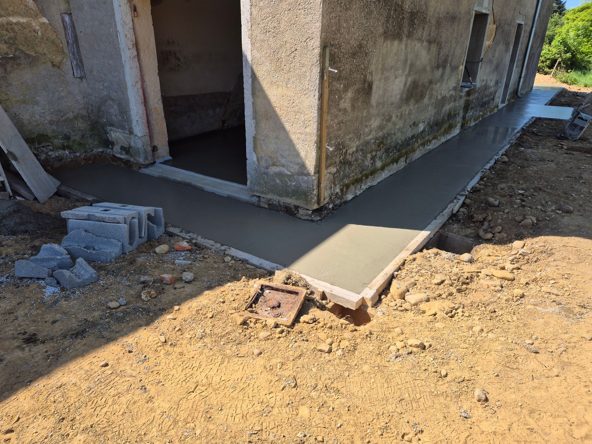 Allée en béton autour d'un bâtiment en construction, avec de la terre et des pierres.