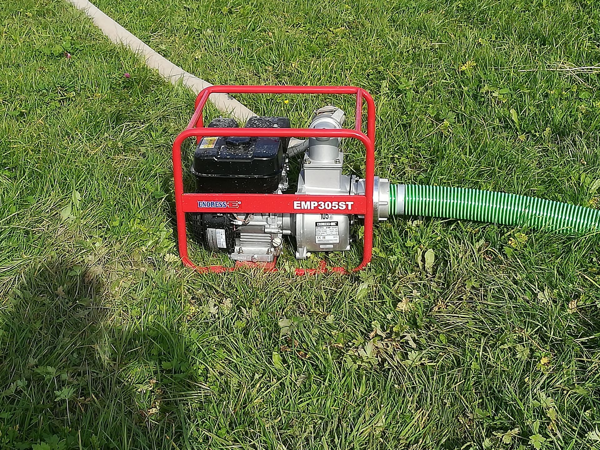 Weingärtner Baumaschinen – Schmutzwasserpumpe mit angeschlossenen Schläuchen auf Wiese