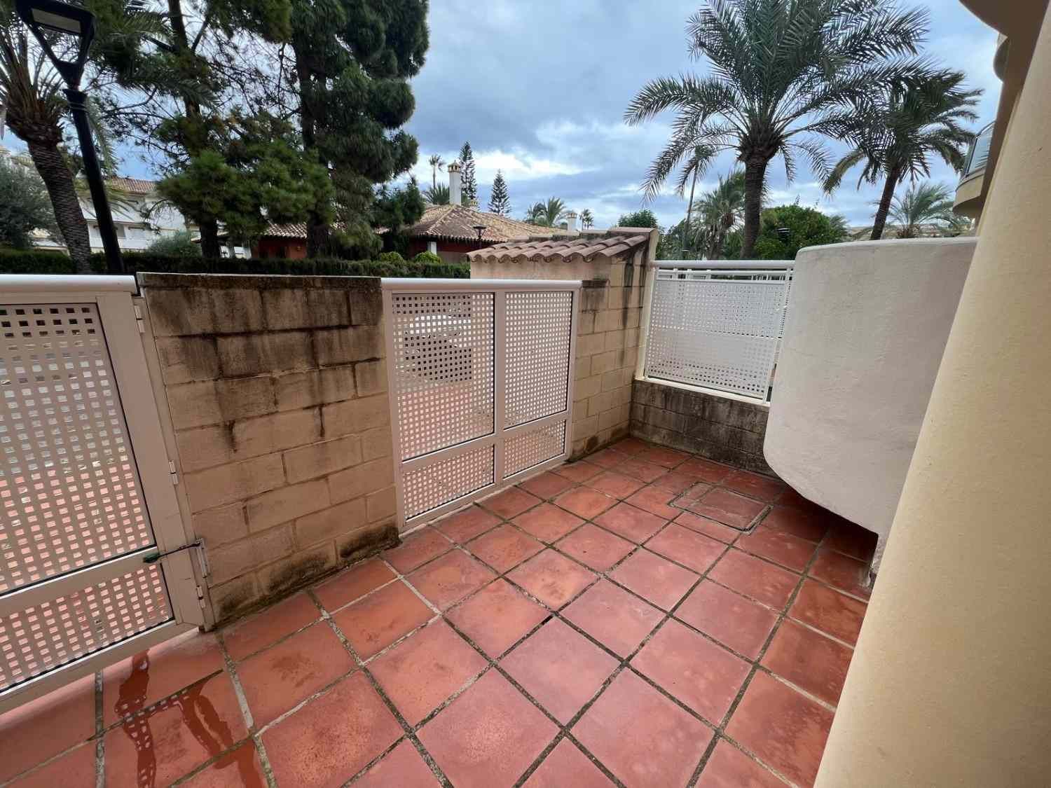 Pequeño patio embaldosado con paredes de celosía blanca y vistas a los árboles bajo un cielo nublado