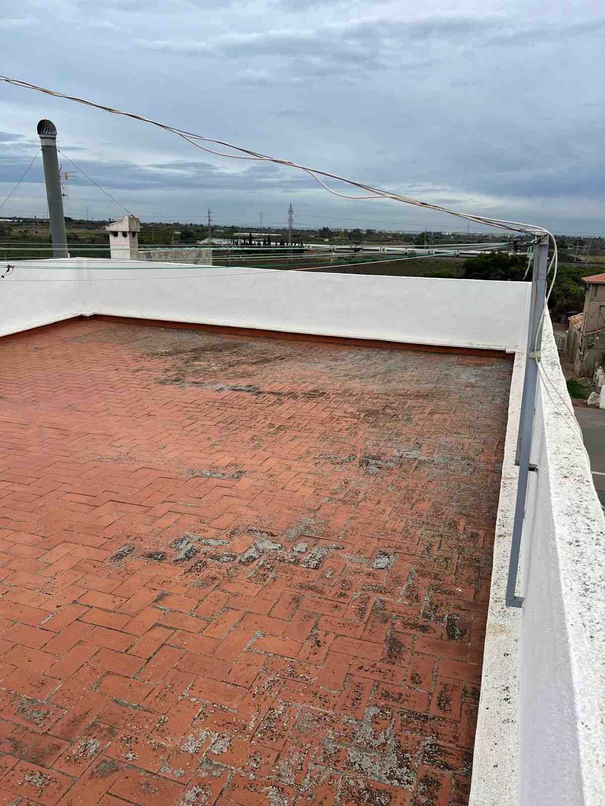 Terraza en la azotea con suelo de ladrillo rojo, paredes blancas y un tendedero bajo un cielo nublado.
