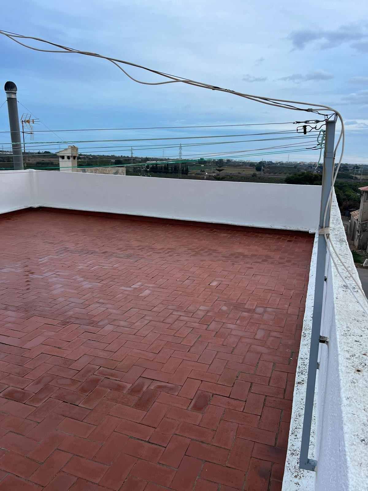 Terraza en la azotea con suelo de ladrillo rojo, paredes blancas y vistas al océano bajo un cielo azul despejado