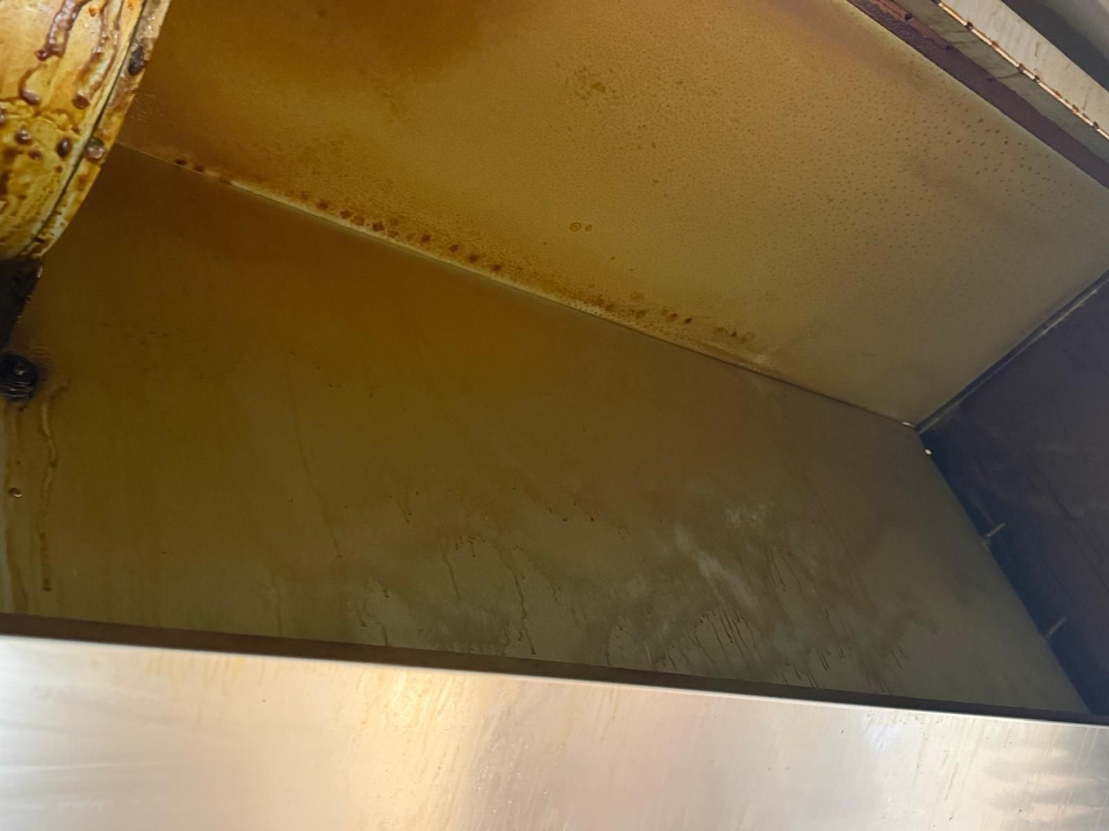Primer plano de una tolva o canaleta de metal amarillo, con óxido y suciedad en el interior