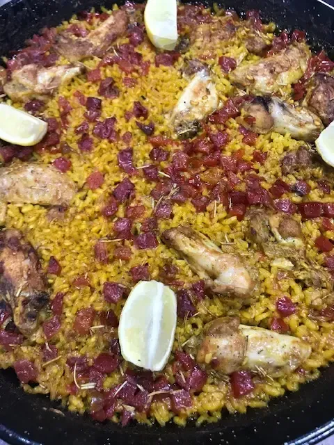 Un primer plano de una paella con pollo y rodajas de limón.