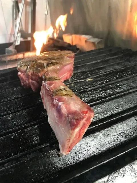 Dos filetes se cocinan en una parrilla con llamas detrás de ellos.