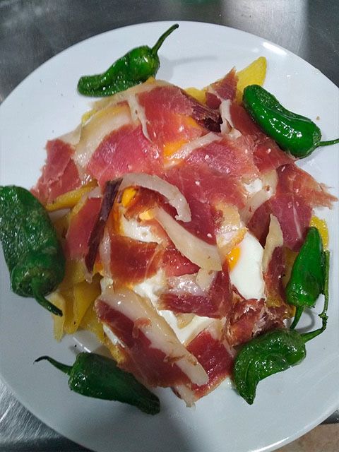 Un plato blanco cubierto con carne, huevos y pimientos.