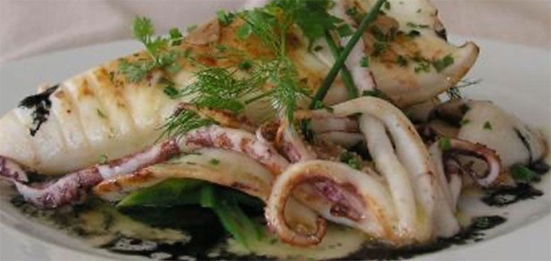 Un plato blanco cubierto con calamares y espinacas sobre una mesa.