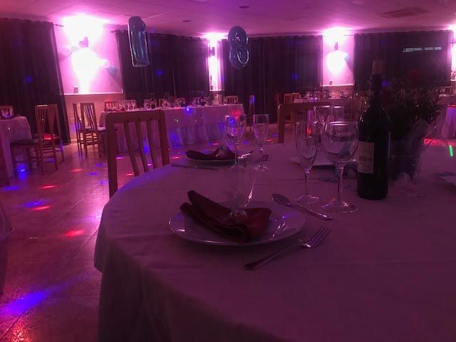 Un comedor con mesas y sillas preparadas para una fiesta con luces moradas.