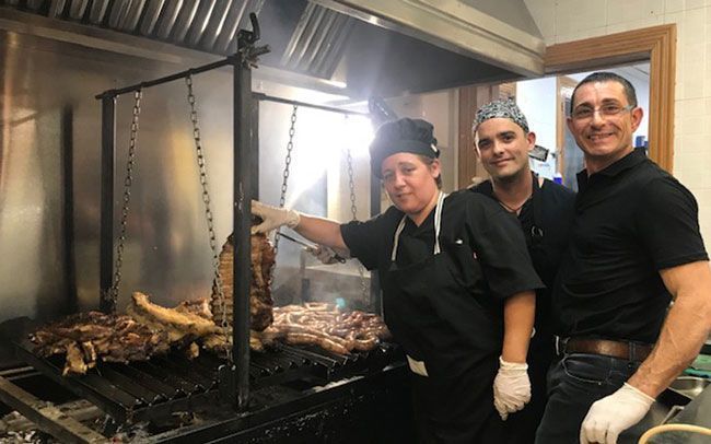 Tres personas están paradas frente a una parrilla con carne.