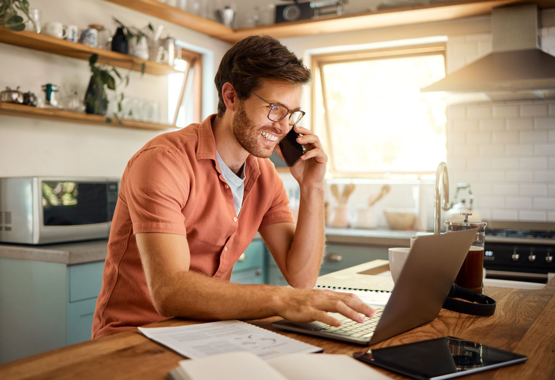 Homme souriant au téléphone devant son ordinateur portable dans la cuisine
