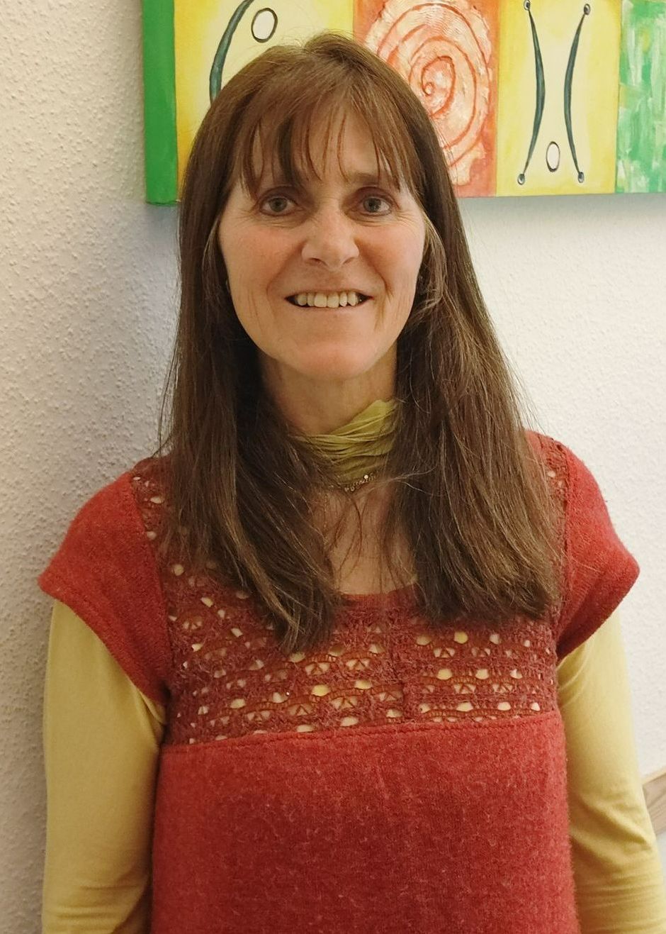 Portrait Marion Buchental - Eine Frau in einem roten Oberteil lächelt vor einem Gemälde