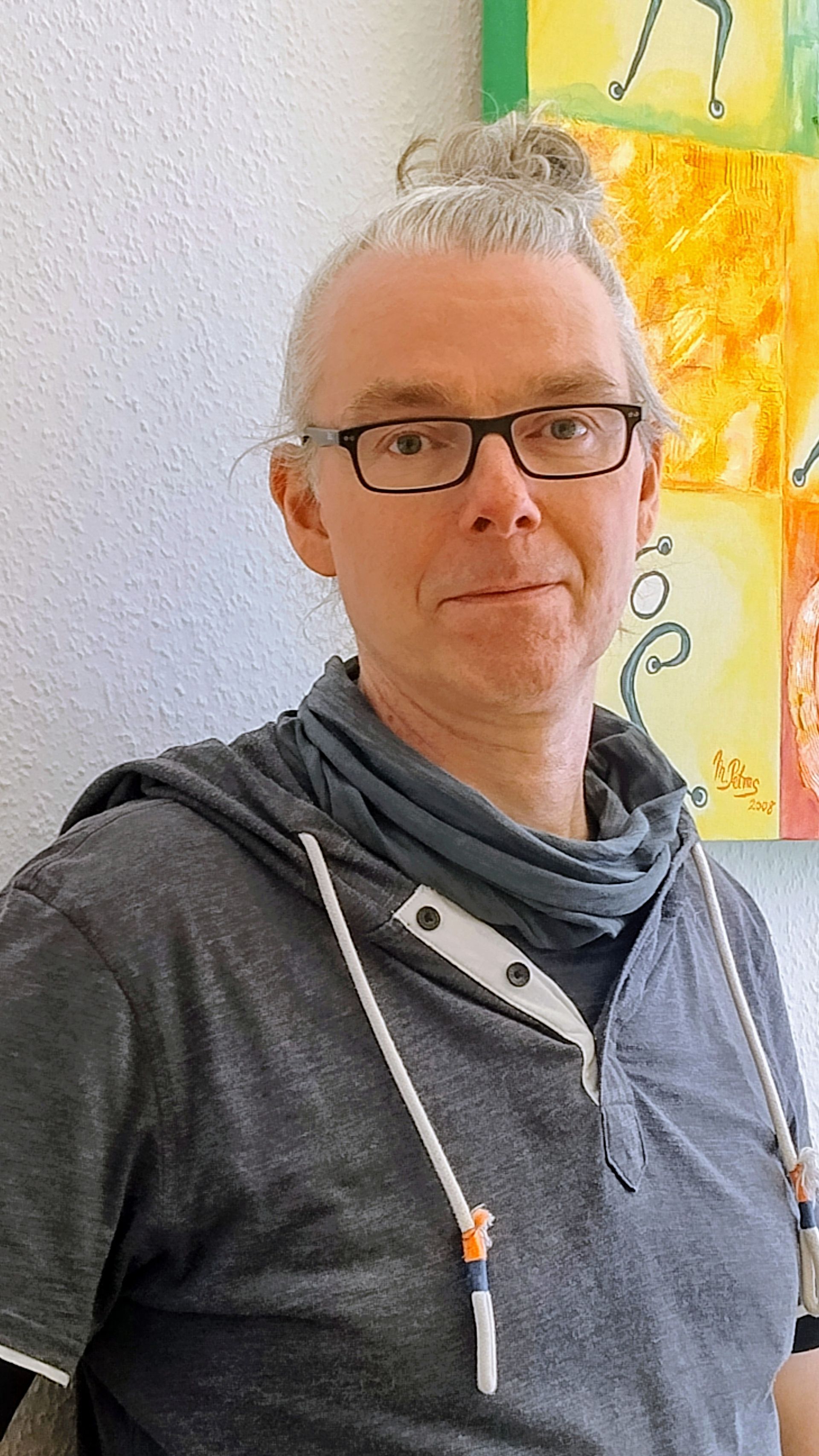 Ein Mann mit Brille und Dutt steht vor einer Wand.