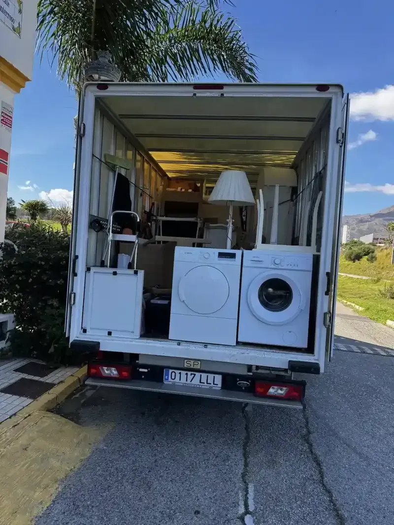 Parte trasera abierta de un camión de mudanzas blanco cargado con electrodomésticos, muebles y cajas