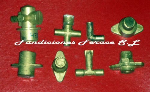 Un montón de herrajes de latón están sobre una superficie roja con las palabras fundiciones ferace sl