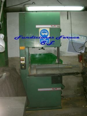 Una sierra de cinta verde está en una habitación con las palabras fundiciones ferace en la pared