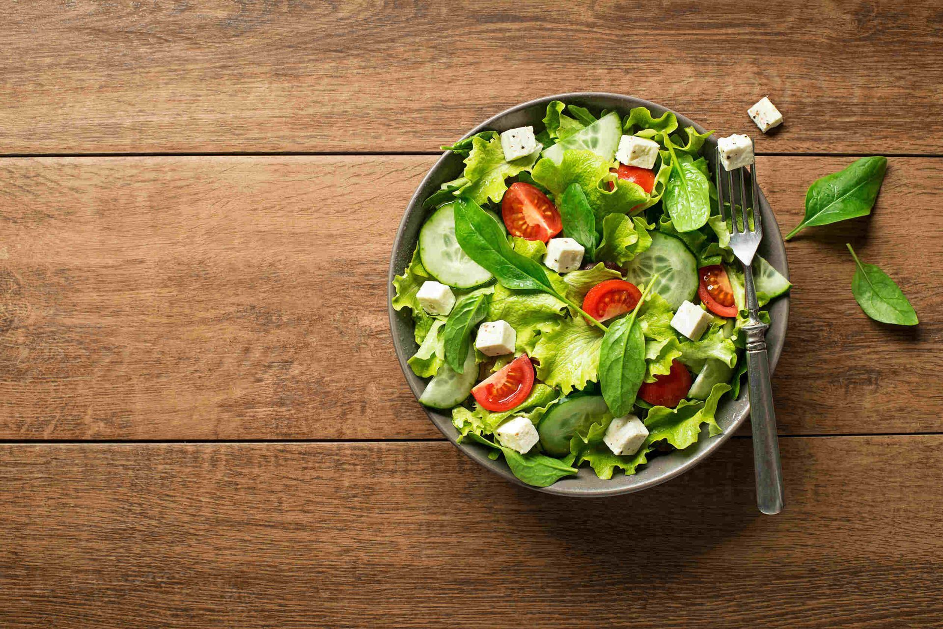 Un tazón de ensalada con tomates, pepinos, lechuga y queso feta en una mesa de madera.