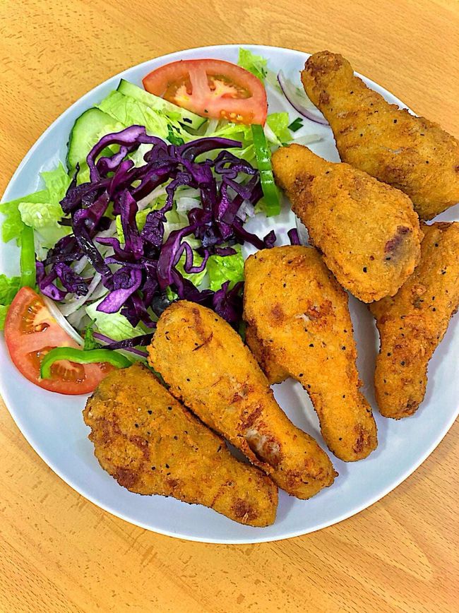 Un plato blanco cubierto con pollo frito y una ensalada sobre una mesa de madera.