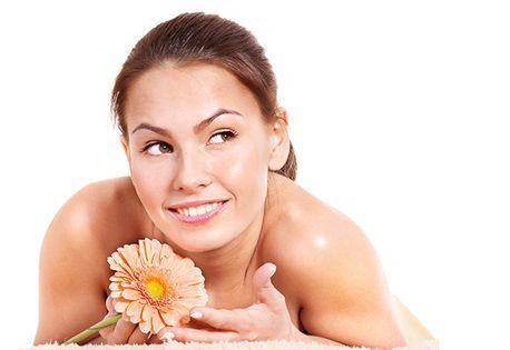Mujer sonriendo, sosteniendo una margarita gerbera color durazno, mirando hacia su derecha, luz suave, aislada sobre blanco.