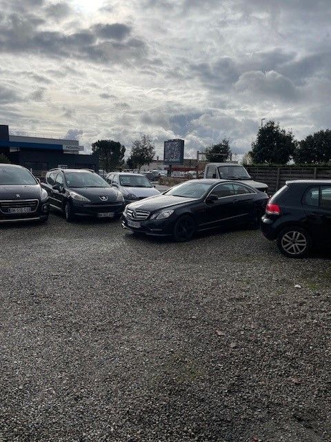 Voitures garées sur un parking en gravier sous un ciel nuageux.