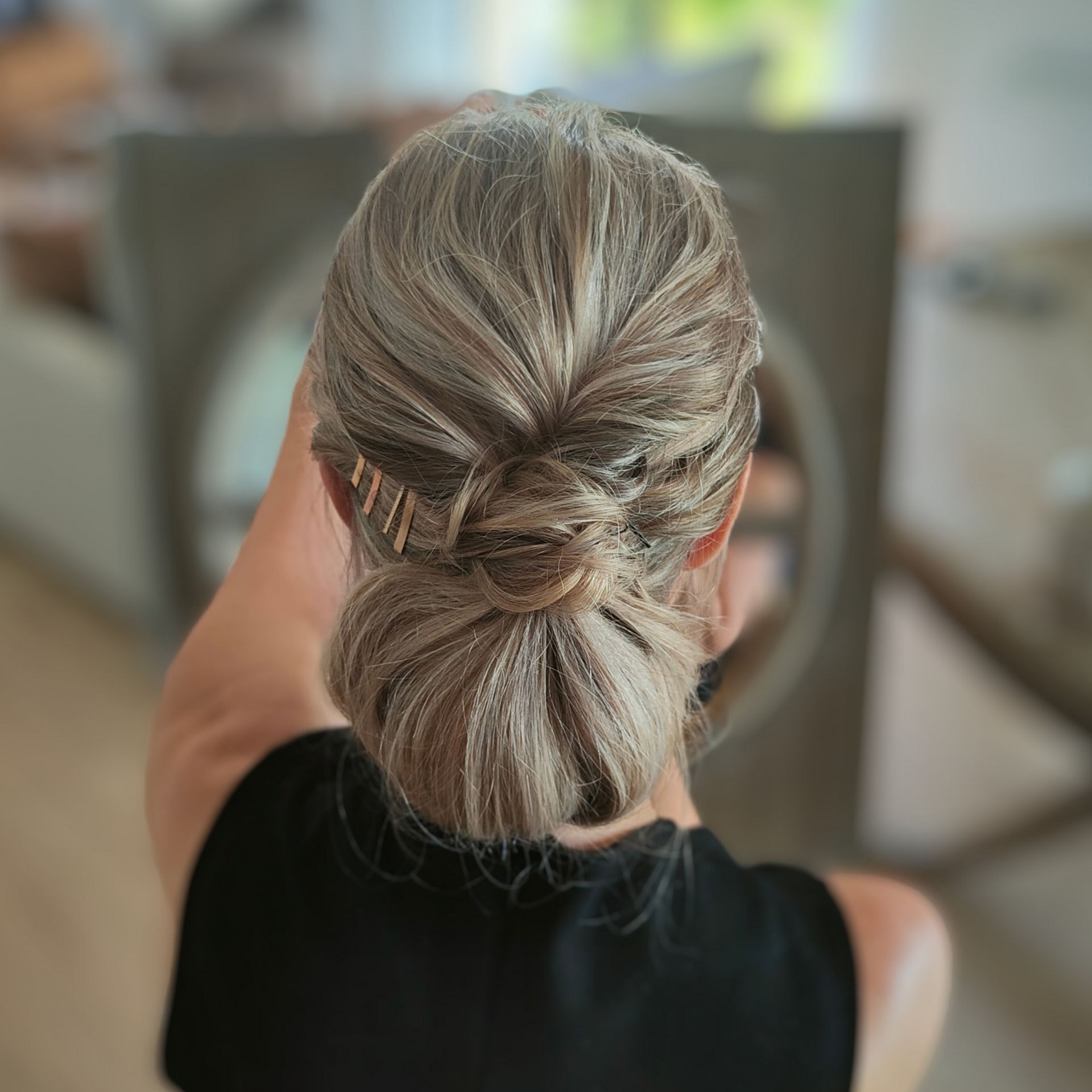 Femme avec une coiffure relevée, ornée d'épingles à cheveux, sur un fond intérieur flou.