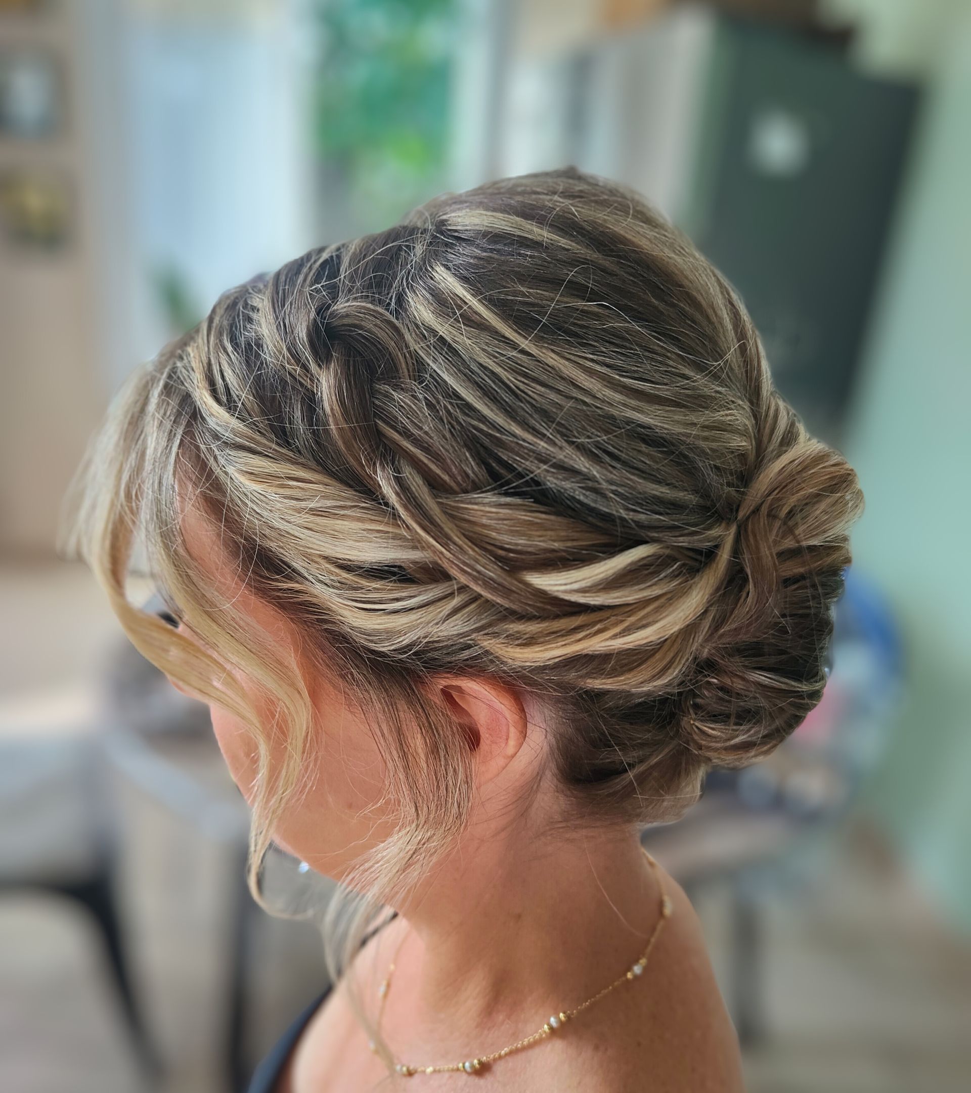 Coiffure relevée avec mèches blondes, torsadée et fixée avec des épingles. Collier en or.