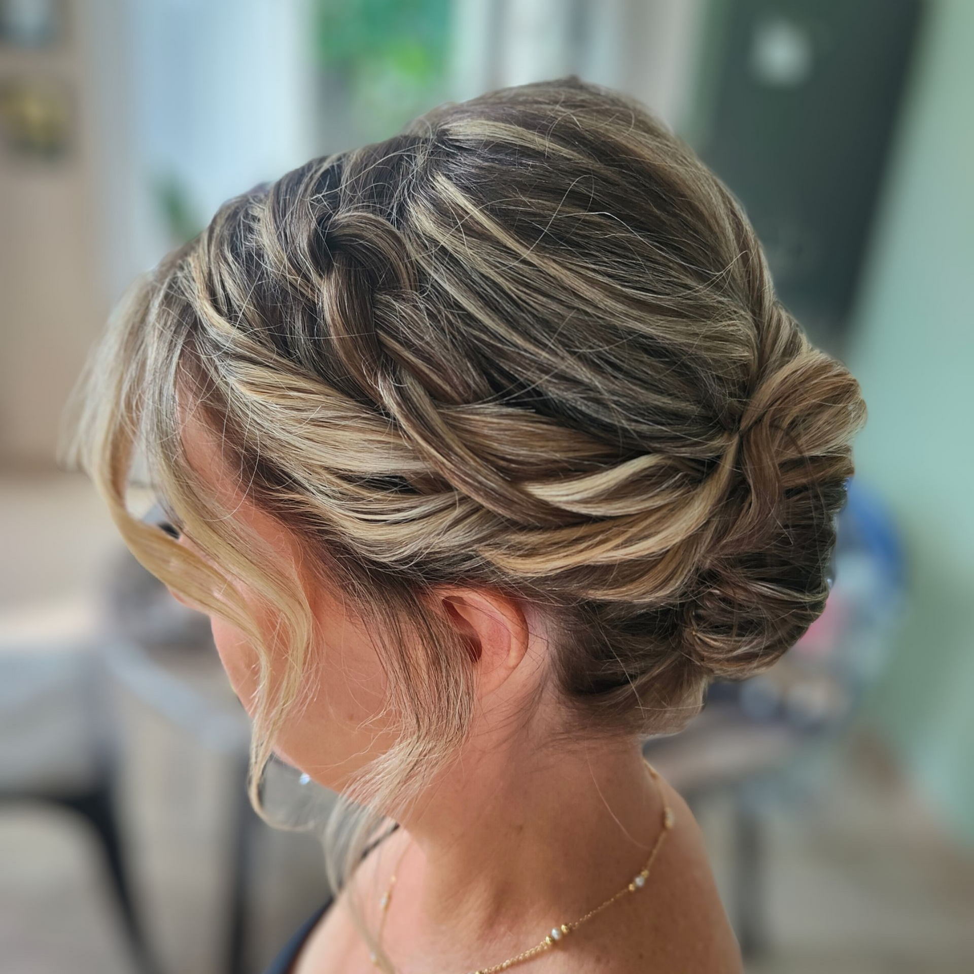 Coiffure relevée avec des tresses et des mèches libres. Cheveux châtain clair avec des mèches et une touche de paillettes.