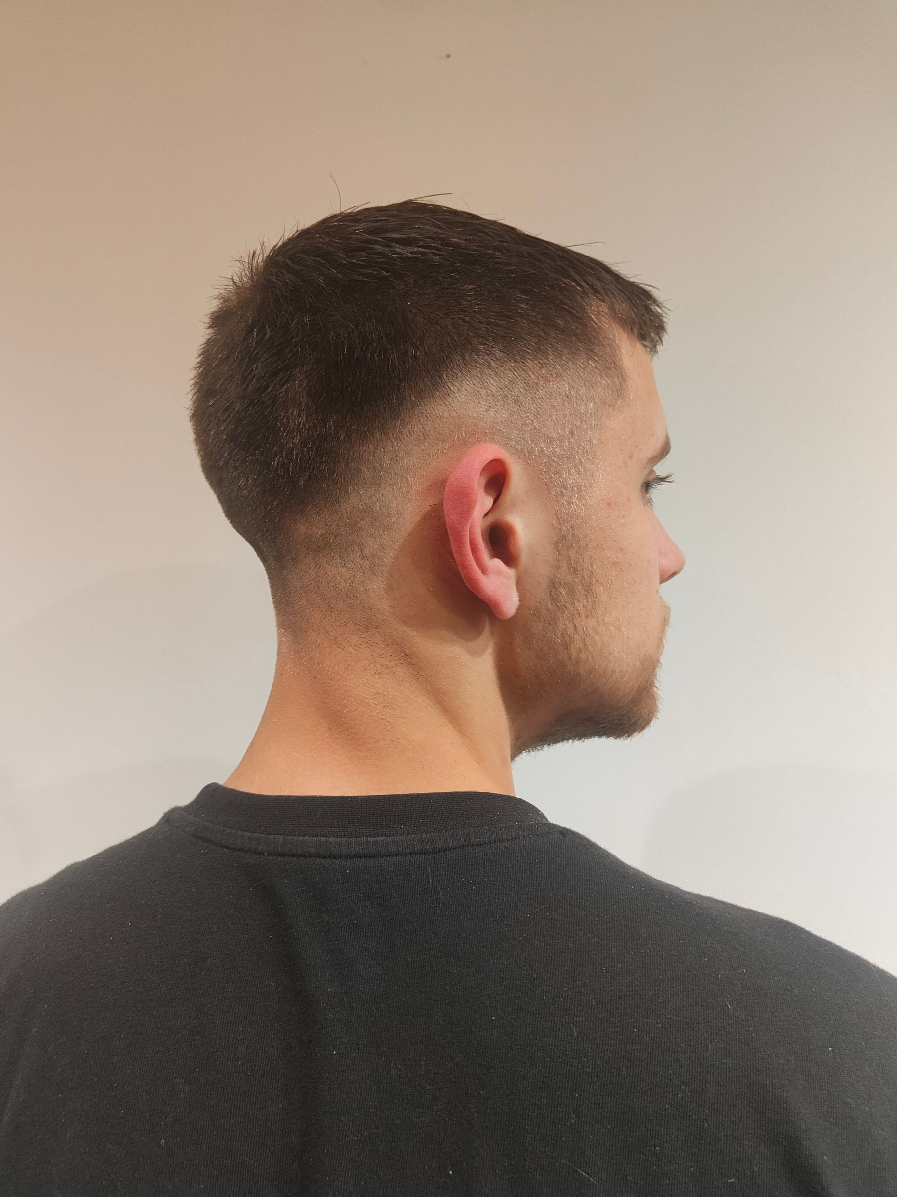 Homme avec une coupe courte, décolorée sur les côtés, vue de profil, sur fond blanc.