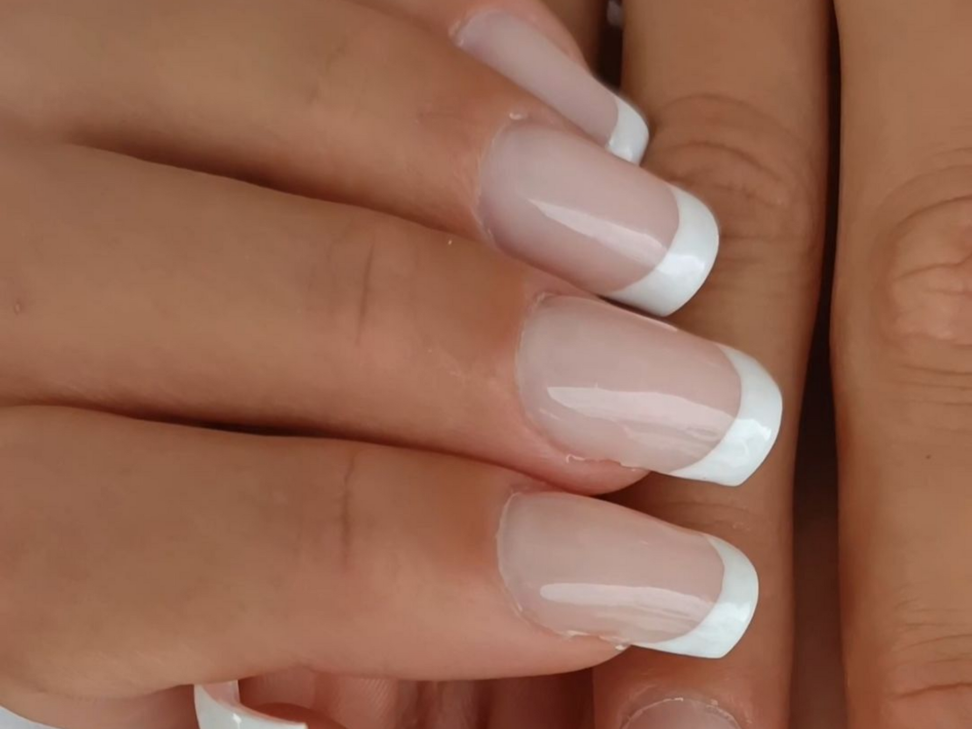 Gros plan de la main avec manucure française sur les ongles : pointes blanches et vernis transparent.
