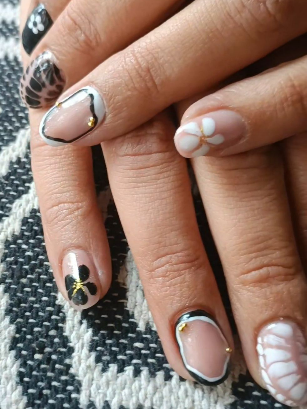 Gros plan de mains manucurées avec divers motifs de nail art, notamment des fleurs et des motifs géométriques.
