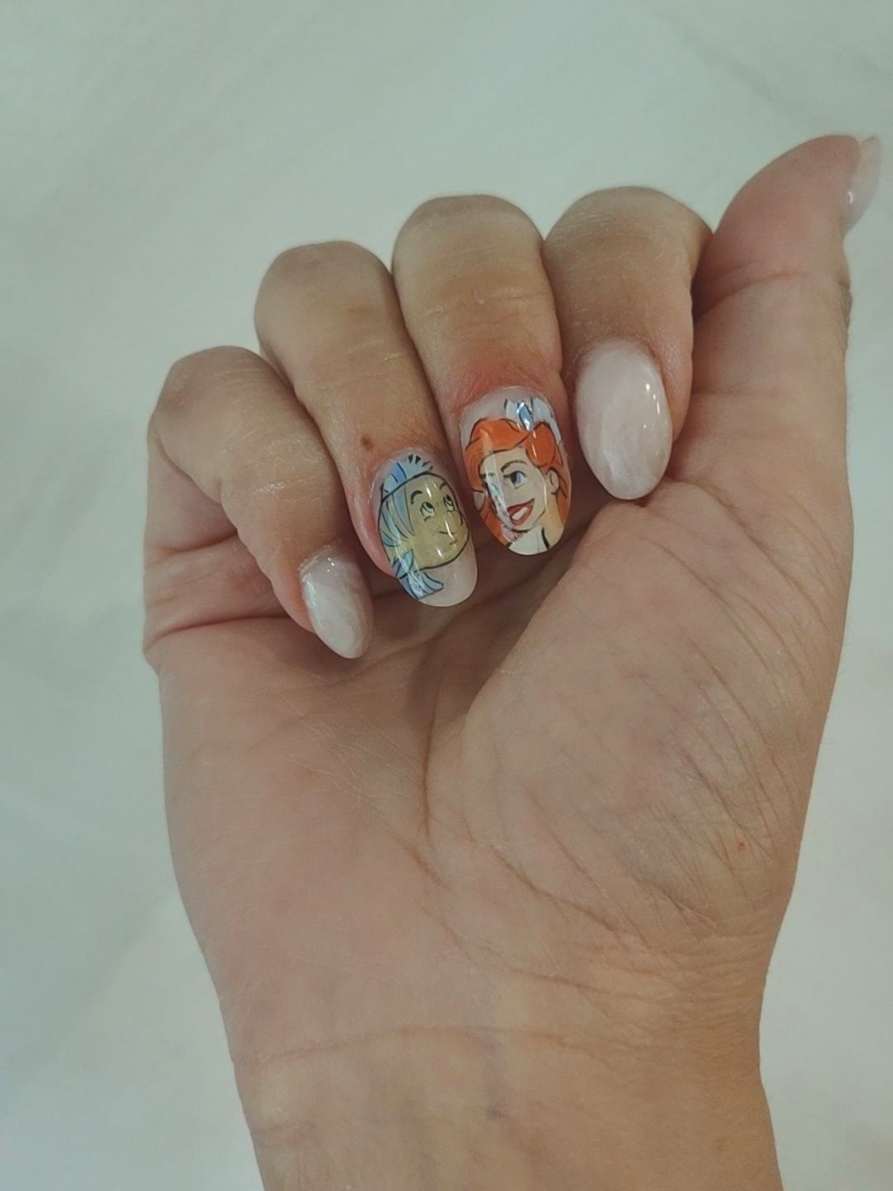 Main avec des ongles peints à l'effigie de personnages de dessins animés. Deux ongles sont ornés de dessins de princesses Disney.