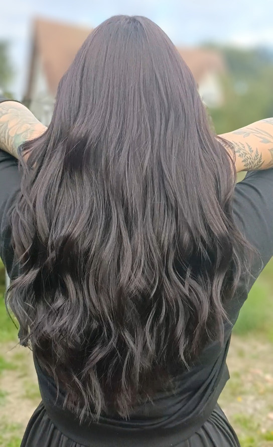 Personne aux cheveux noirs et tatouée, bras levés. Extérieur avec arrière-plan flou.