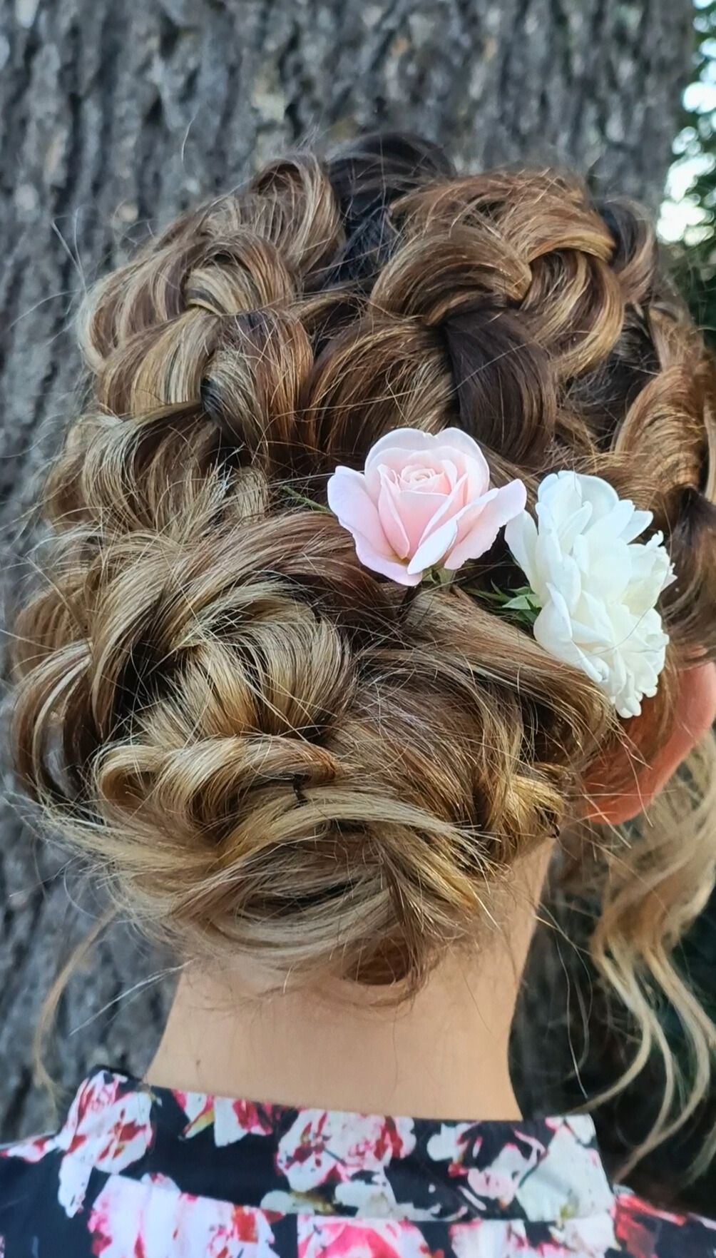 Coiffure chignon tressée avec des fleurs roses et blanches.