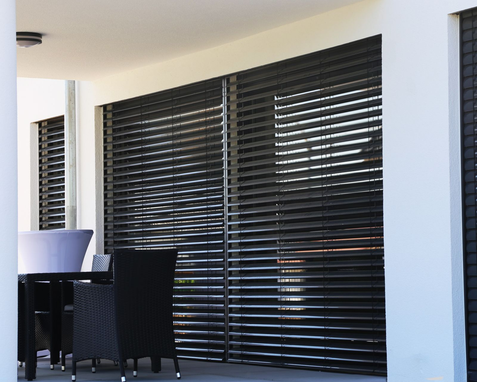 Terrasse extérieure avec brise-soleil à lames noires, table et chaises sous un auvent blanc