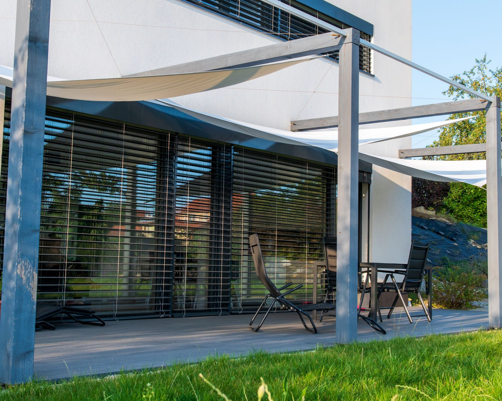 Patio avec toiles d'ombrages blanches et chaises noires devant des baies vitrées équipées de BSO