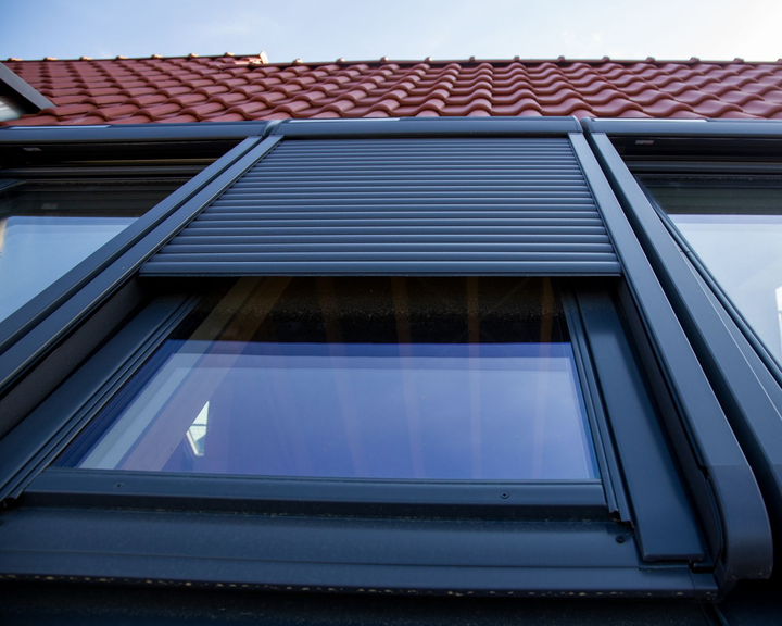 Volet roulant à lames grises recouvrant partiellement une fenêtre