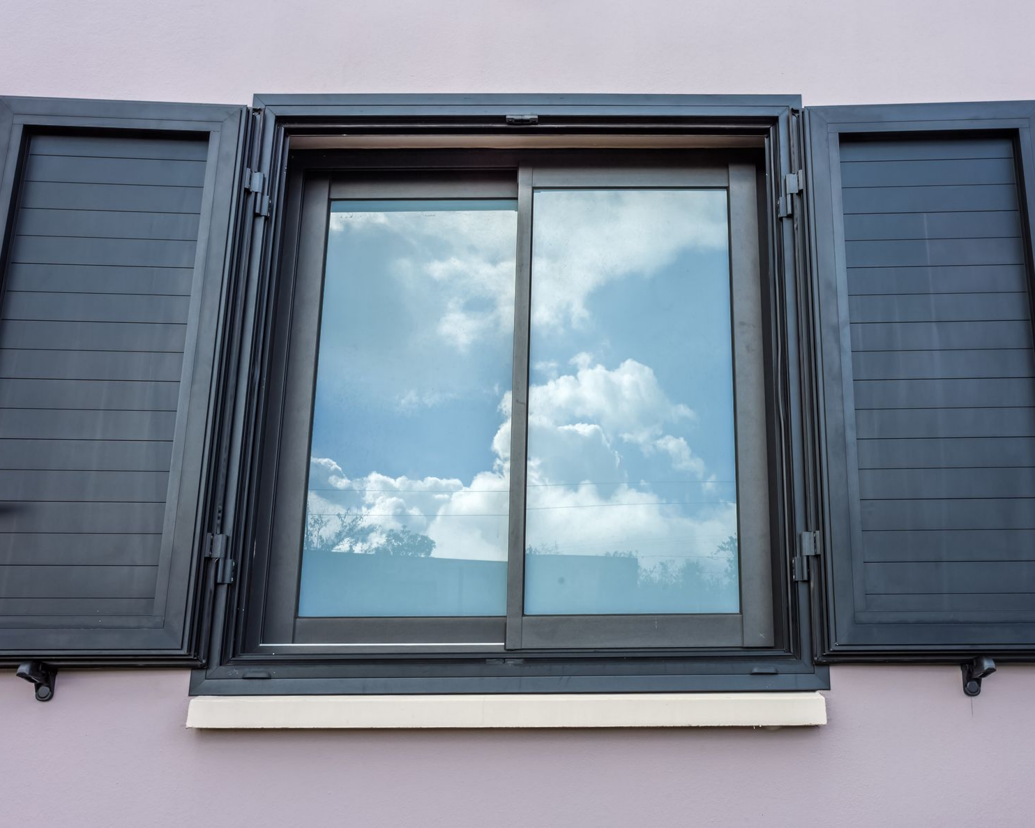 Fenêtre avec volets battants , les vitres reflétant le ciel et des nuages blancs