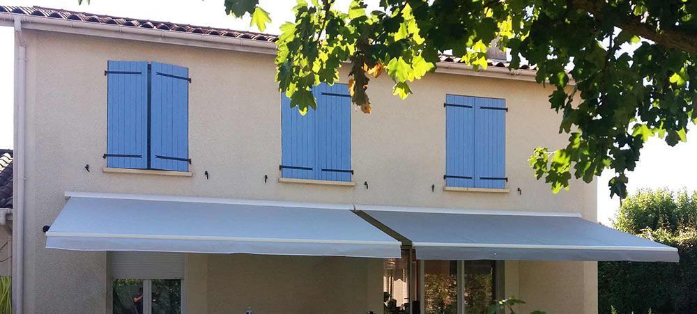 Trois volets battant bleu et store gris sur une façade de maison