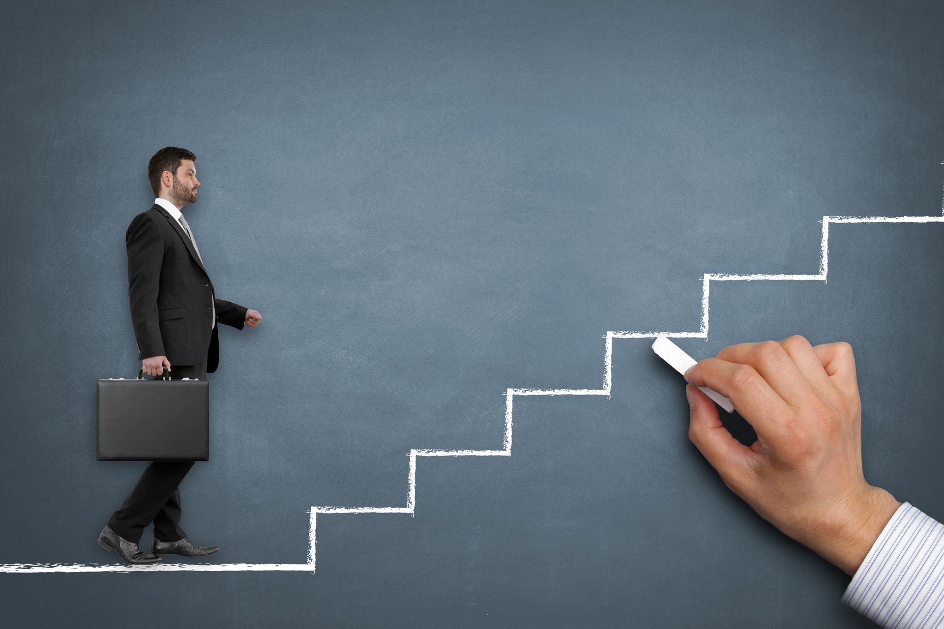 Ein Mann im Anzug geht eine mit Kreide gezeichnete Treppe hinauf, eine Hand zeichnet die nächste Stufe an eine dunkle Wand, er hält einen Aktenkoffer.