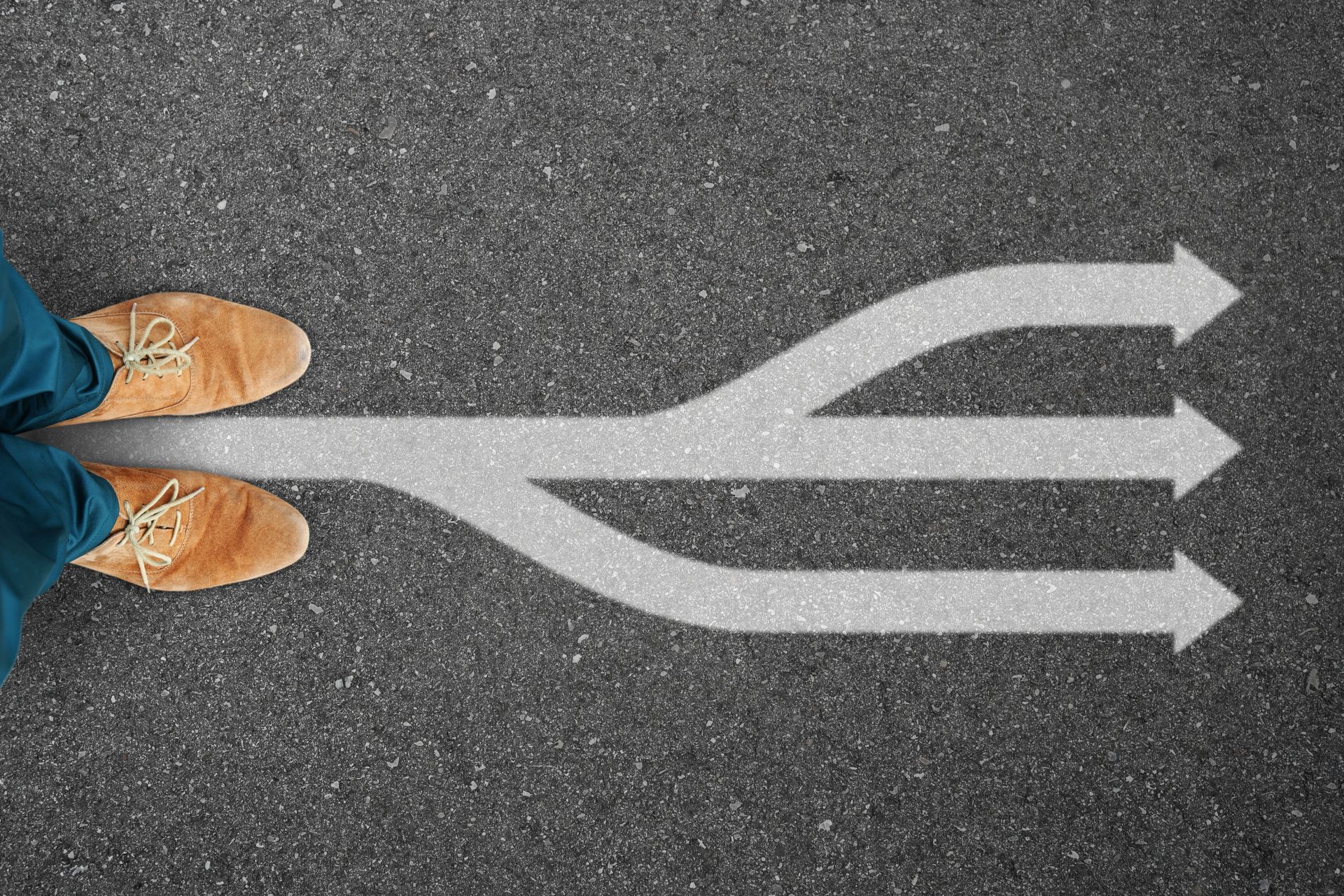 Schuhe stehen auf Asphalt, wo sich ein Weg in drei Pfeile gabelt.