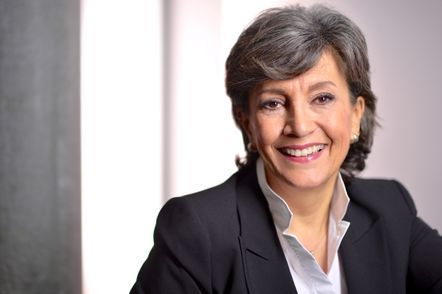 Frau in schwarzem Anzug und weissem Hemd lächelt vor einem verschwommenen weiss-grauen Hintergrund.