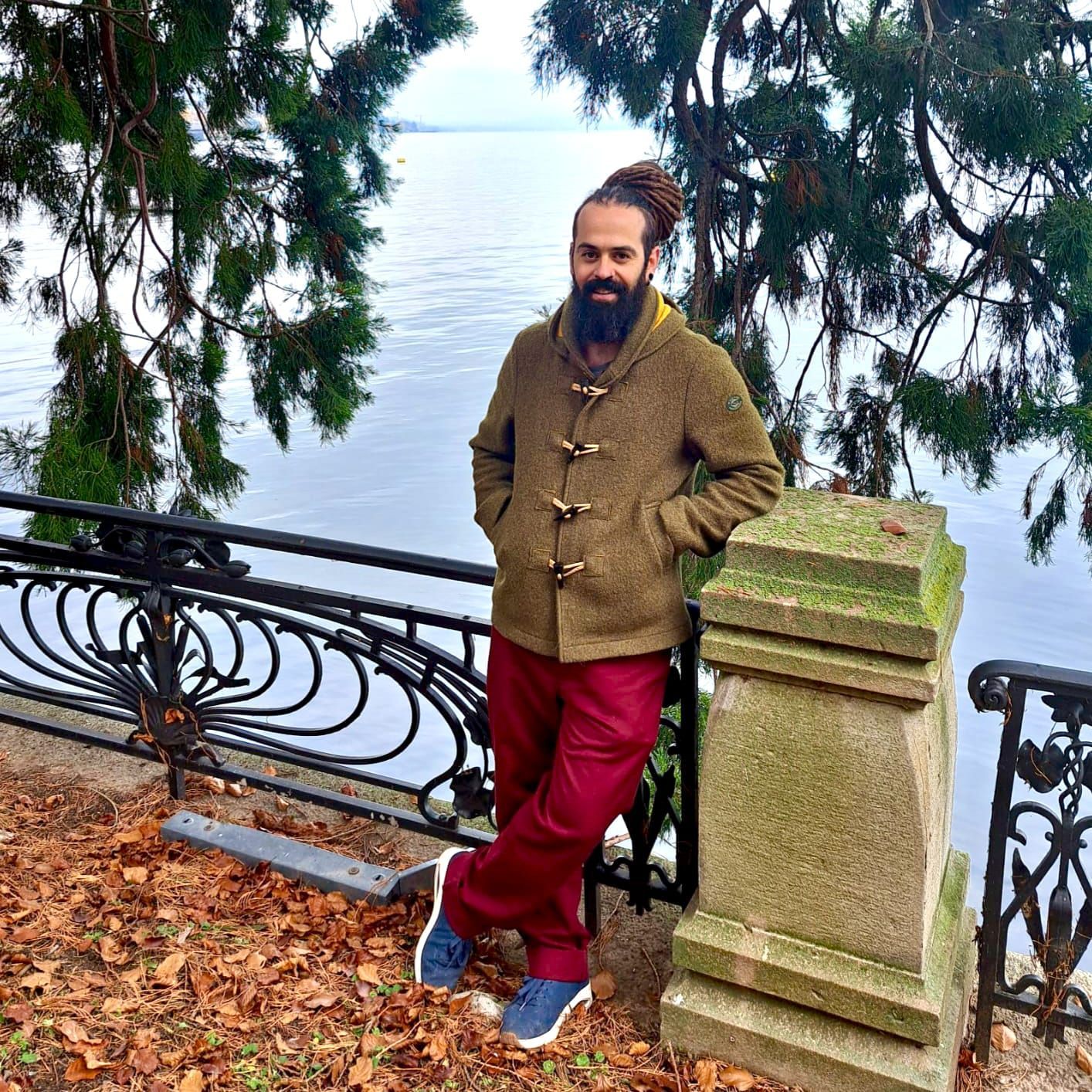 Ein Mann mit Sonnenbrille, weissem Hemd und blauen Shorts steht an einem sonnigen Tag an einer Steinmauer mit Blick auf den Ozean.