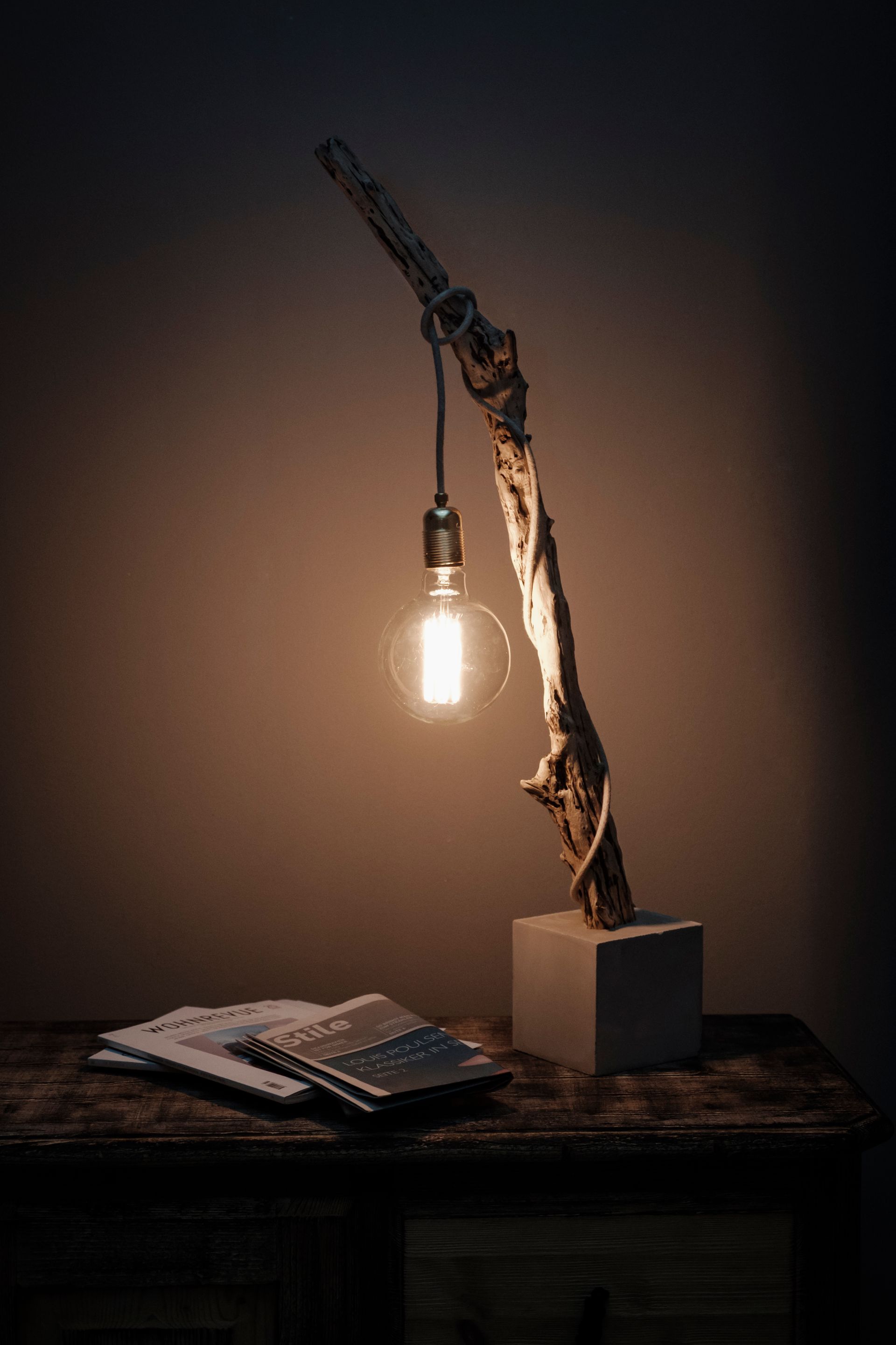 Rustikale Lampe aus Treibholz mit einer hängenden Edison-Glühbirne auf einem dunklen Holztisch.
