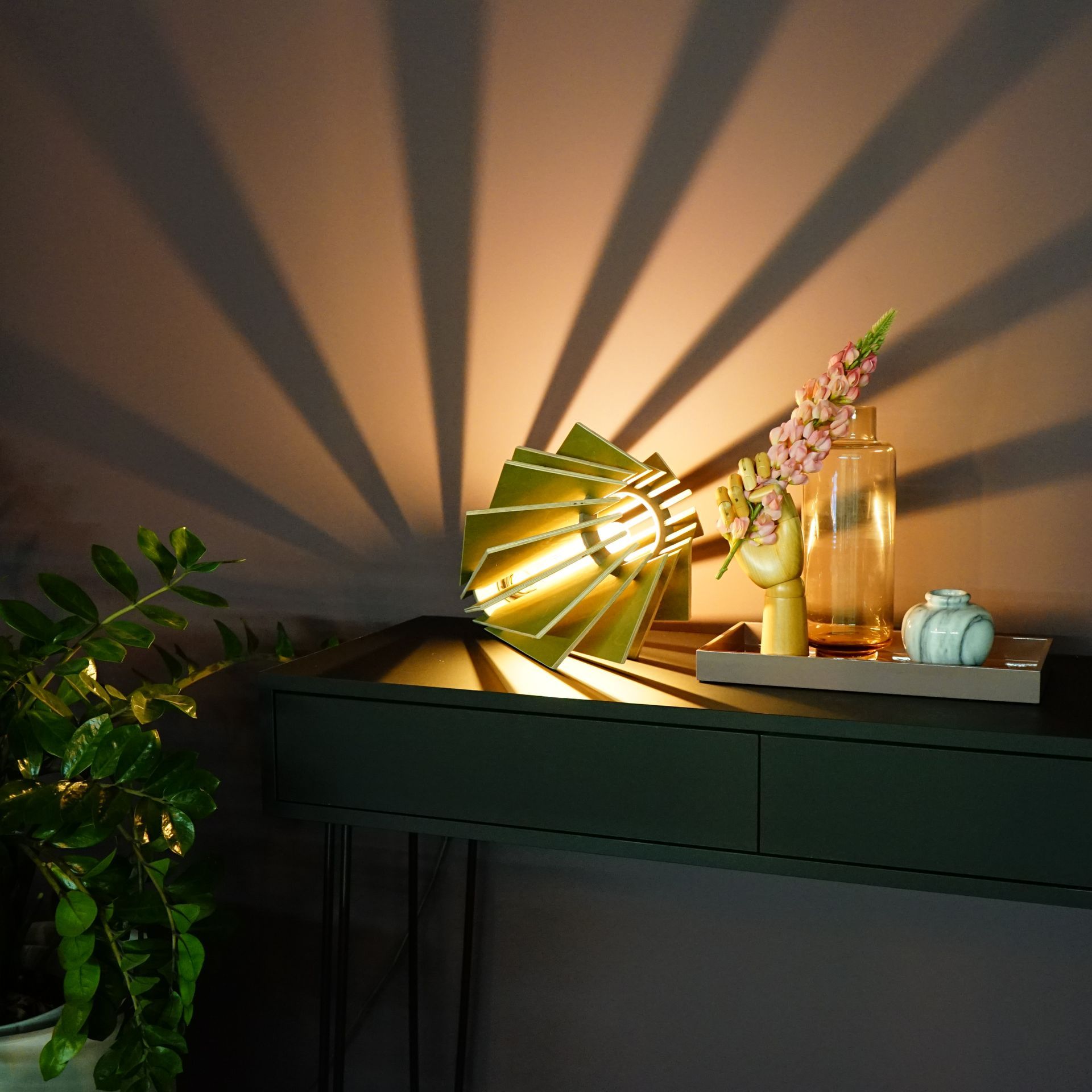 Eine sternförmige Leuchte an einer dunklen Wand, die Kissen und eine Zimmerpflanze beleuchtet.