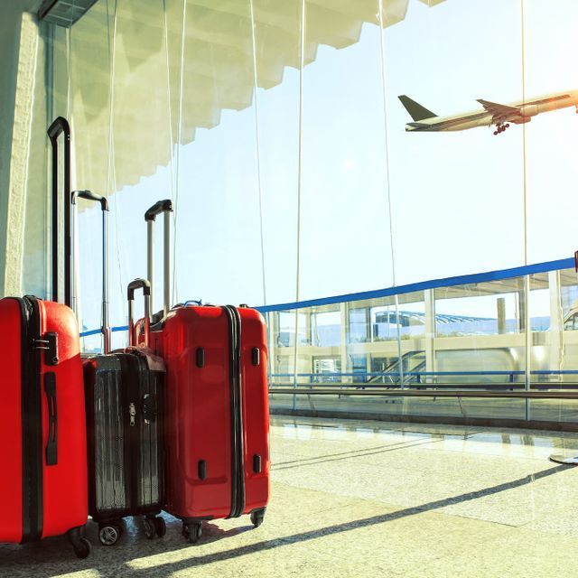 Valises rouges dans un terminal d'aéroport, avion au décollage en arrière-plan. Journée ensoleillée.