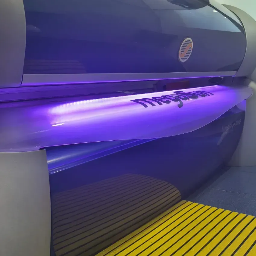 Cama de bronceado con iluminación violeta, toldo abierto y esterilla de rayas amarillas.
