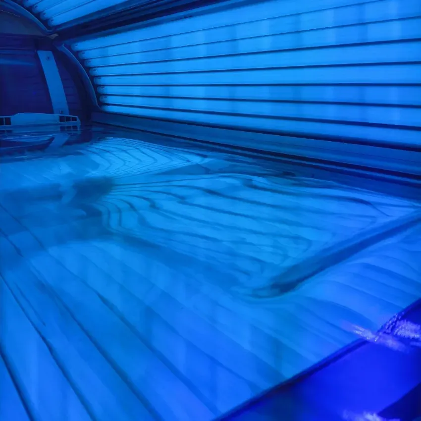 Interior de cabina de bronceado con iluminación azul, superficie acrílica a rayas y dosel curvo.