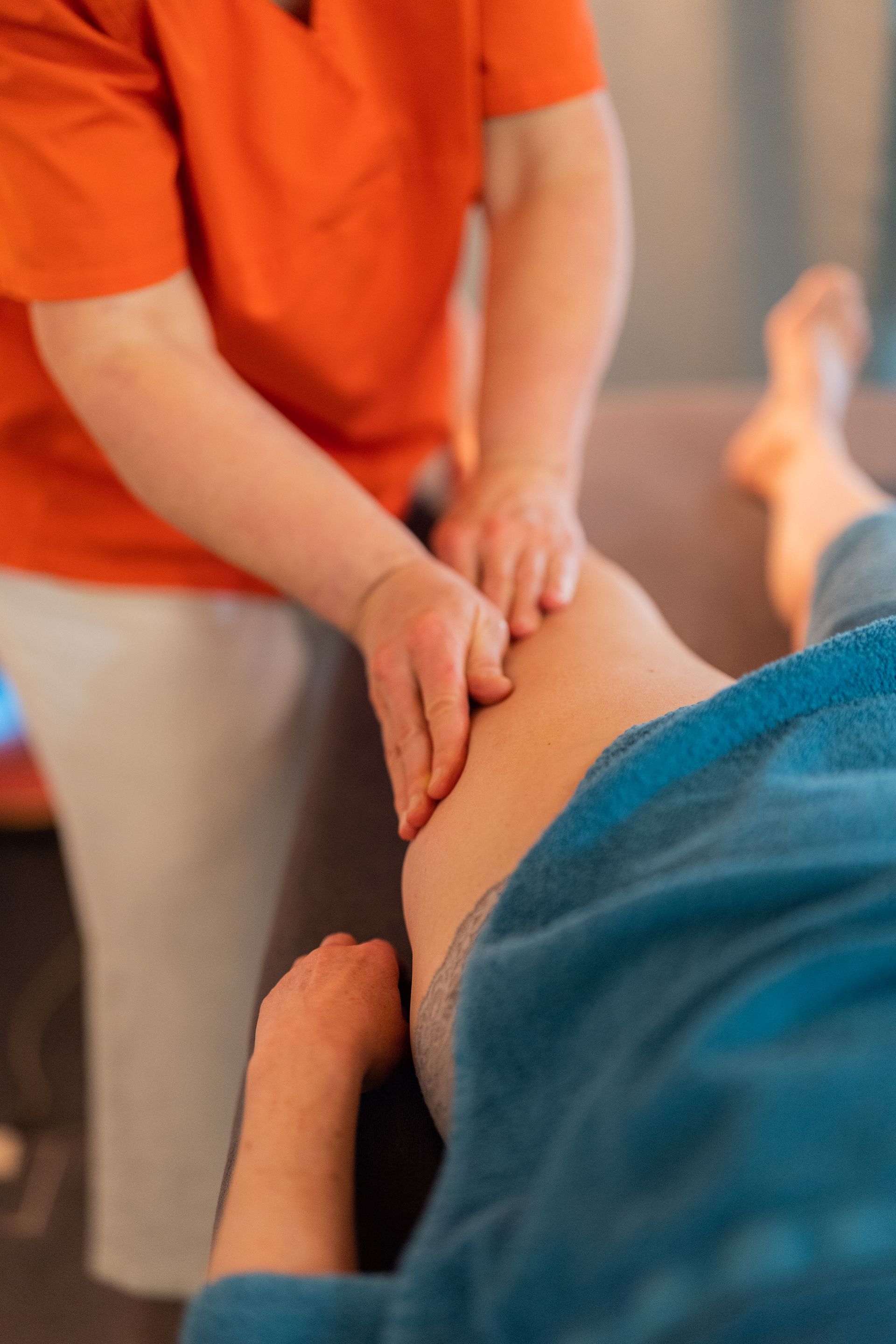 Personne recevant un massage des jambes ; thérapeute en chemise orange.