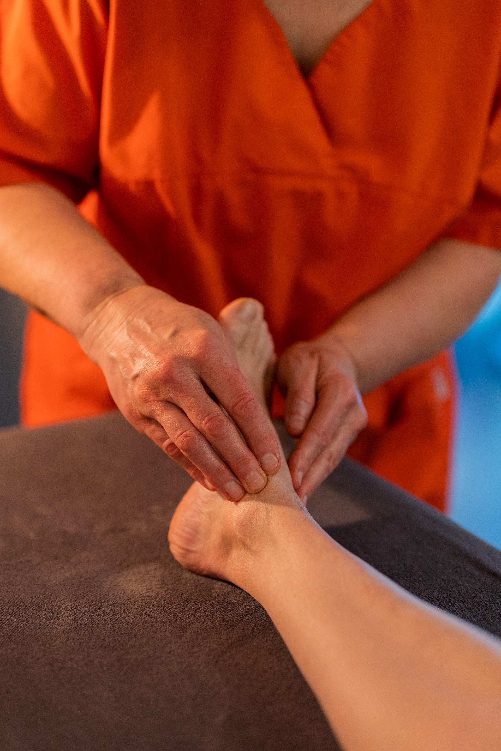 Des mains massent le dos d'une personne, vêtue d'un t-shirt orange et allongée sur une serviette bleue.
