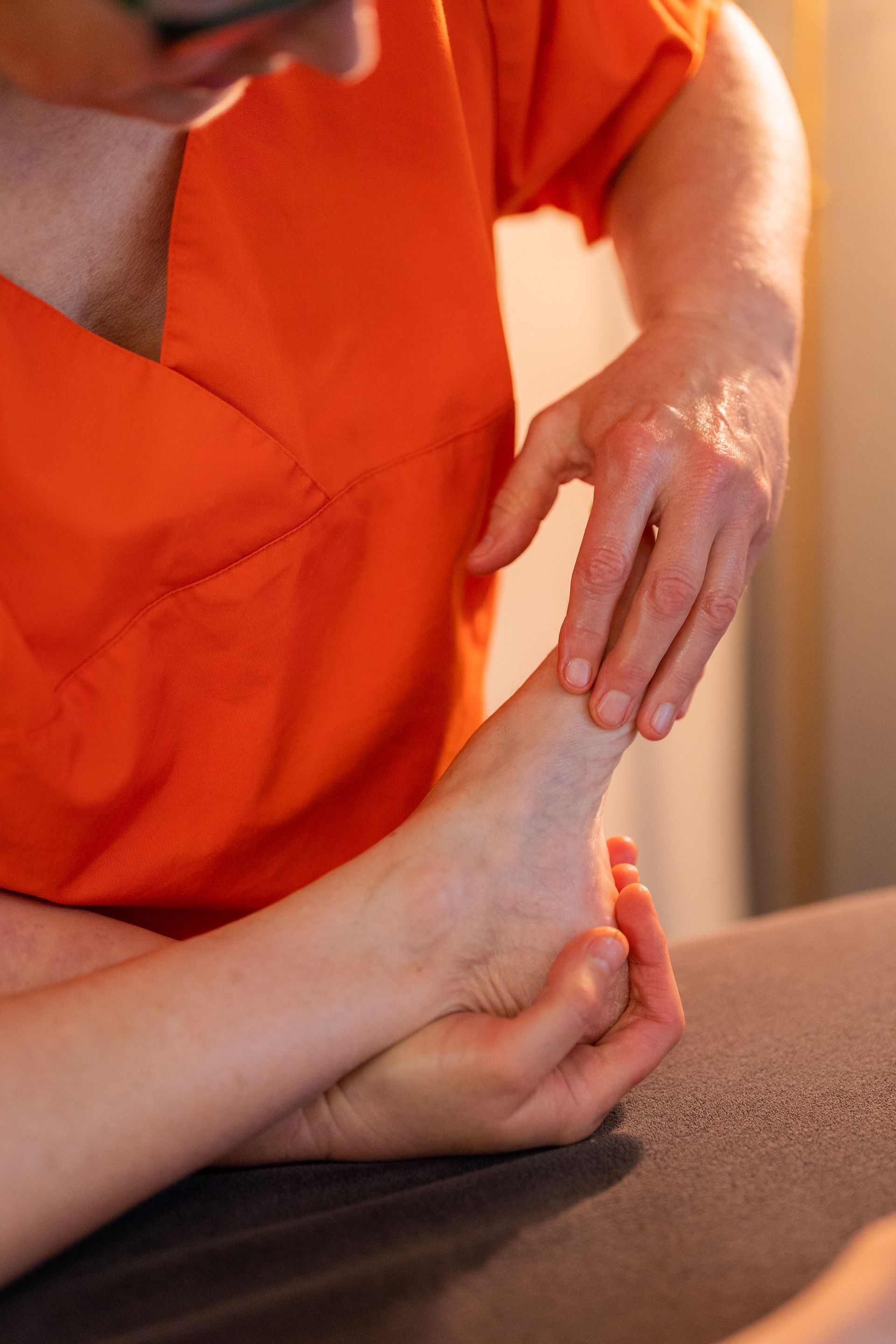 Une personne en blouse orange masse un pied, à l'intérieur, sur une table.