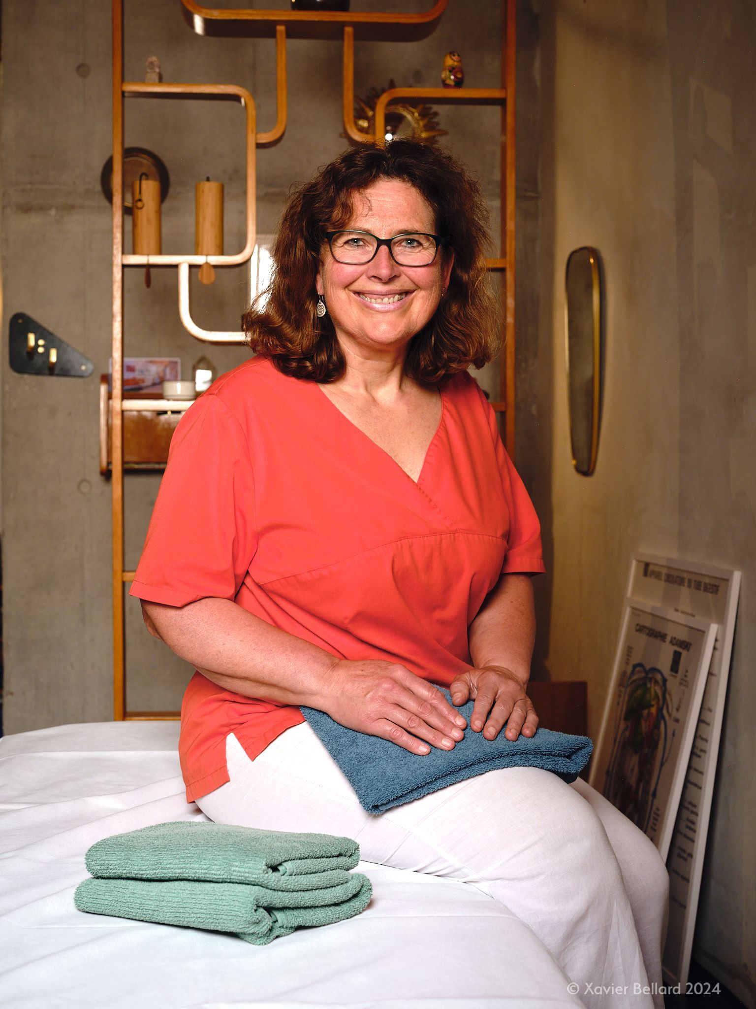 Une personne reçoit un massage des épaules sur une table de massage. Les mains du thérapeute sont posées sur ses épaules ; les yeux du patient sont fermés, enveloppé dans une serviette bleue.